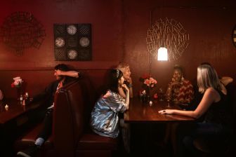 Group of adults enjoying drinks at a dimly lit bar booth with artistic decor.